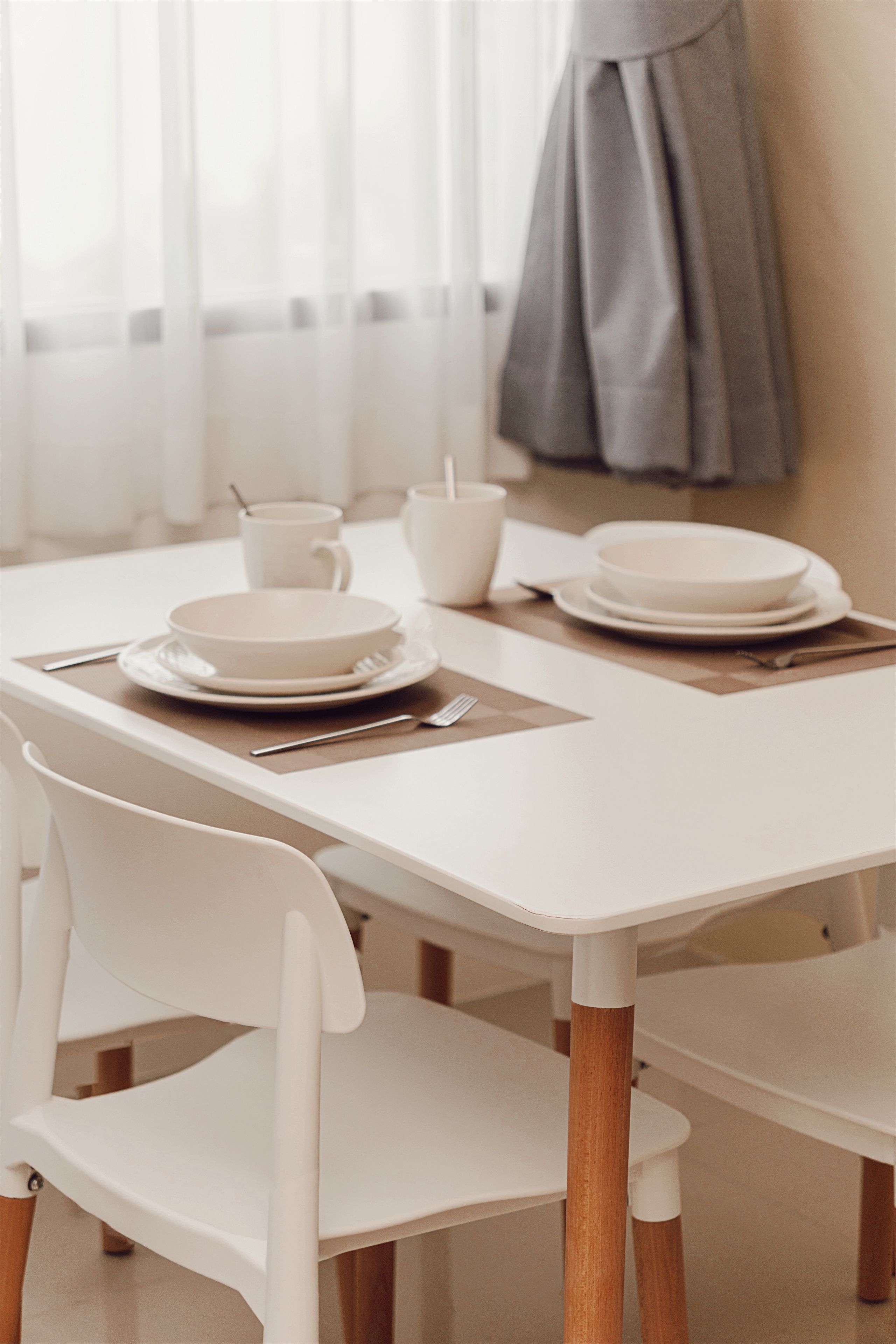 A dining table with white chairs, plates, and cutlery.
