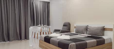 A modern bedroom with a wooden bed, grey curtains, a white table with chairs, and a grey armchair.