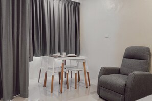 A modern room with a dining table and chairs, a grey armchair, and grey curtains.