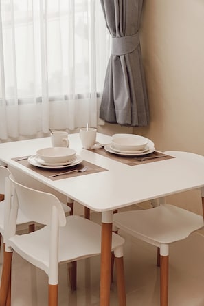 A dining table with white chairs and a white tablecloth, set with plates, bowls, and cups.