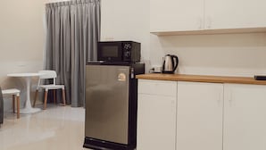Een compacte kitchenette met een koelkast, magnetron en waterkoker, een kleine eettafel met stoelen en een grijze gordijn.