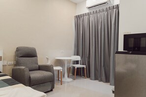 A hotel room with a grey armchair, a small white table, a TV, and grey curtains.