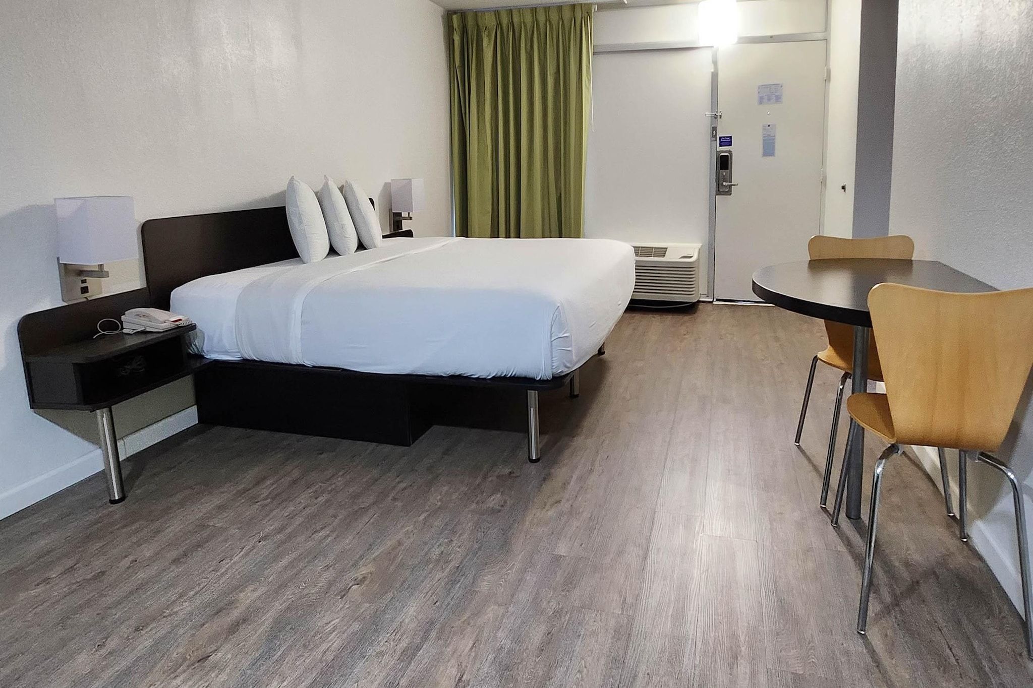 A hotel room with a bed, bedside table, chair, and a small table with a chair.
