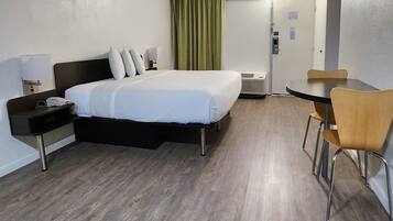 A hotel room with a bed, bedside table, chair, and a small table with a chair.