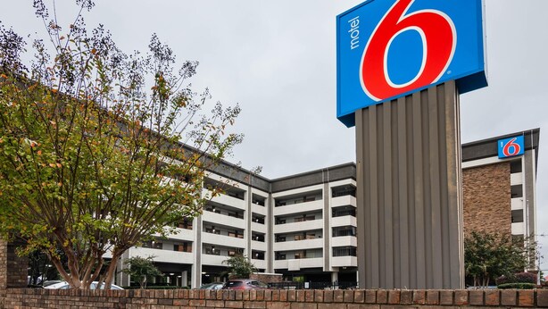 Ein Motel mit einem gut sichtbaren Schild mit der Zahl 6, einer Parkgarage und einer Ziegelwand.