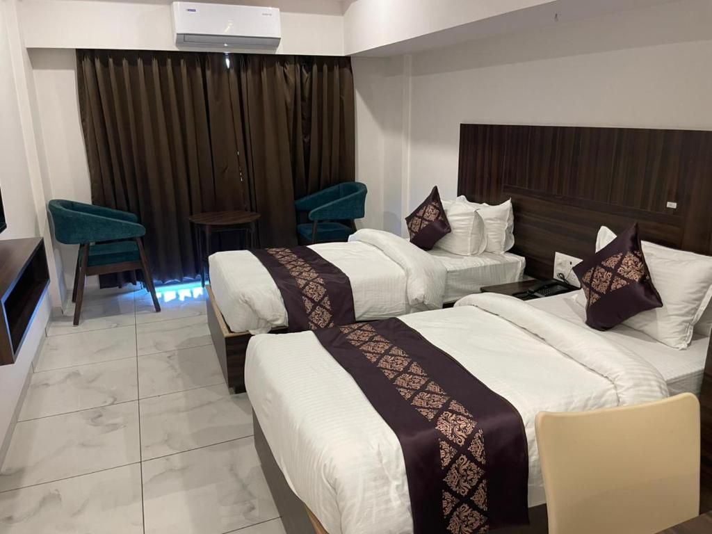 A hotel room with two beds, a small table, two chairs, and a curtain backdrop.