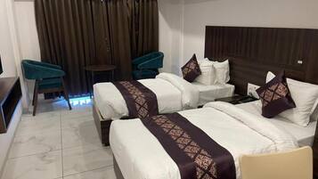 A hotel room with two beds, a small table, two chairs, and a curtain backdrop.