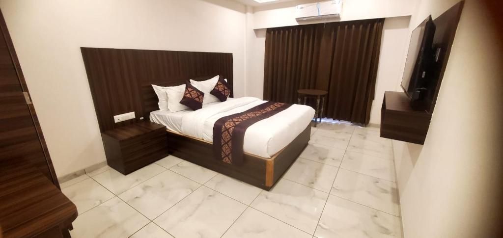 A hotel room with a bed, bedside tables, a TV, and a curtain.