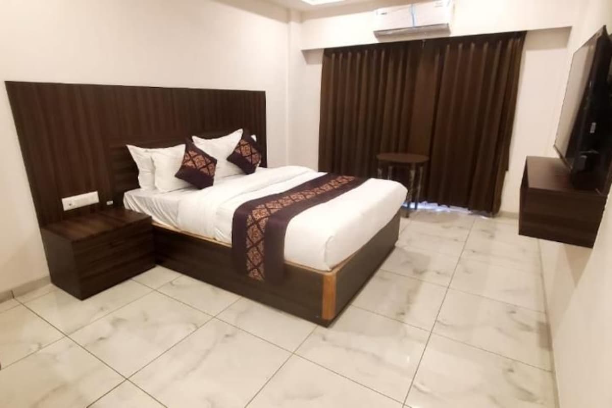 Une chambre d’hôtel avec un lit, des tables de chevet, une télévision et un rideau.