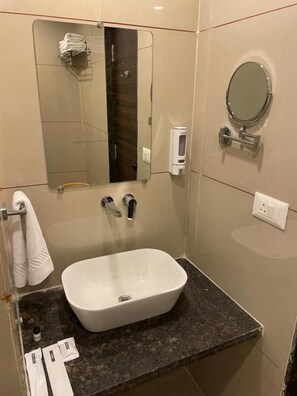 A bathroom with a white sink, a mirror, and a towel rack. - Hotel Mahavir (ANKLESHWAR)