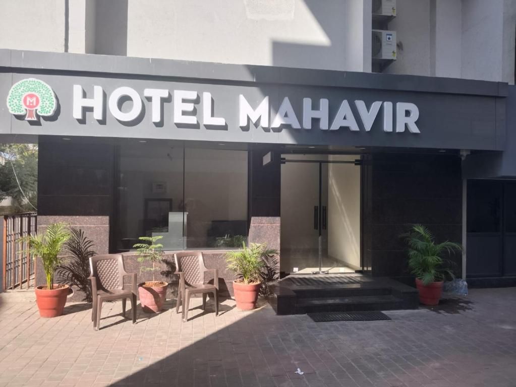 A hotel entrance with a sign reading 'HOTEL MAHAVIR,' outdoor seating with potted plants, and a modern building facade.