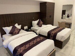 A hotel room with two beds, a wardrobe, a desk, and a mirror. - Hotel Mahavir (ANKLESHWAR)
