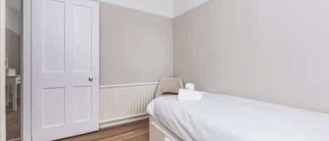Une chambre avec un lit simple, une porte fermée et un radiateur.