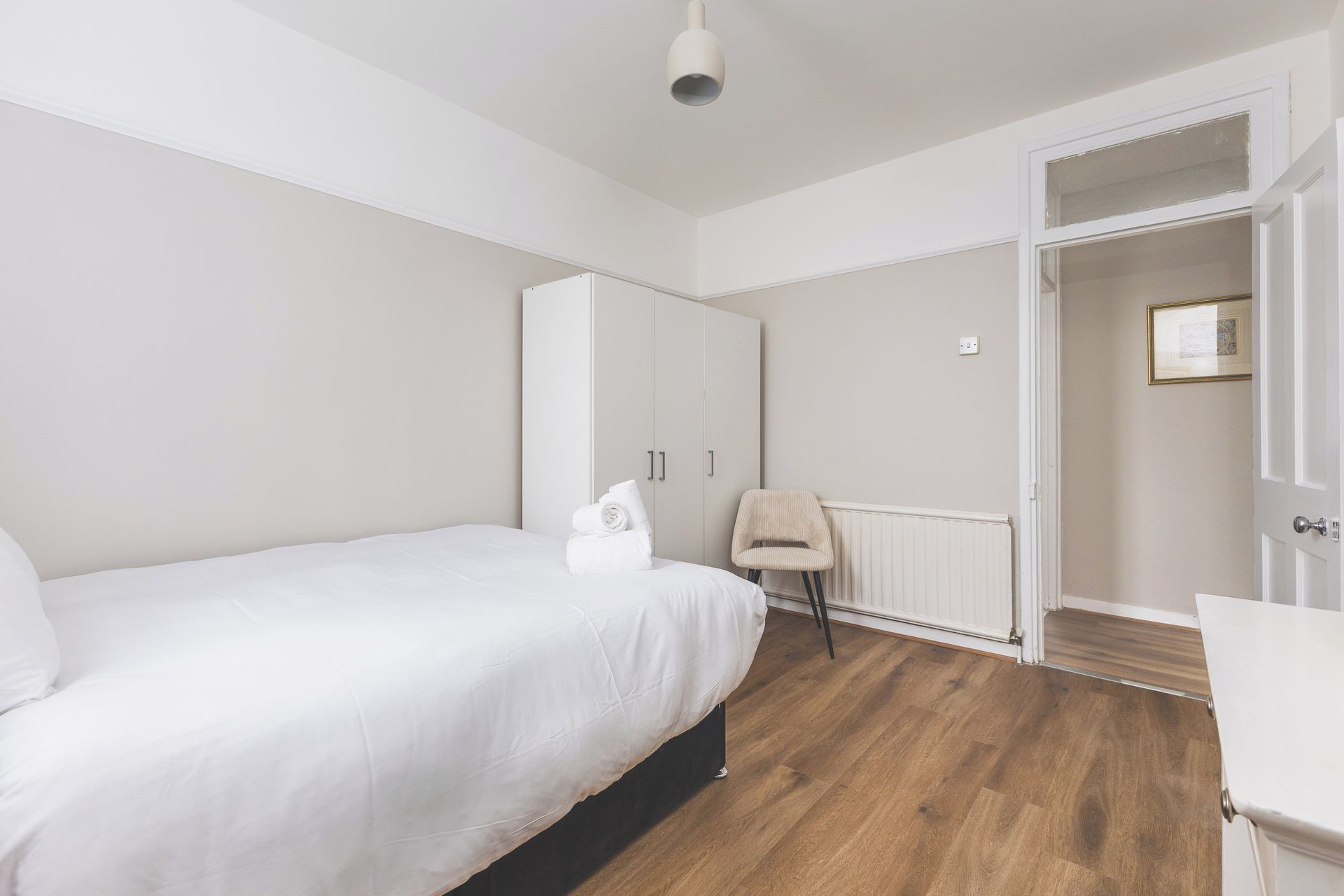 A bedroom with a bed, a chair, a wardrobe, and a radiator.