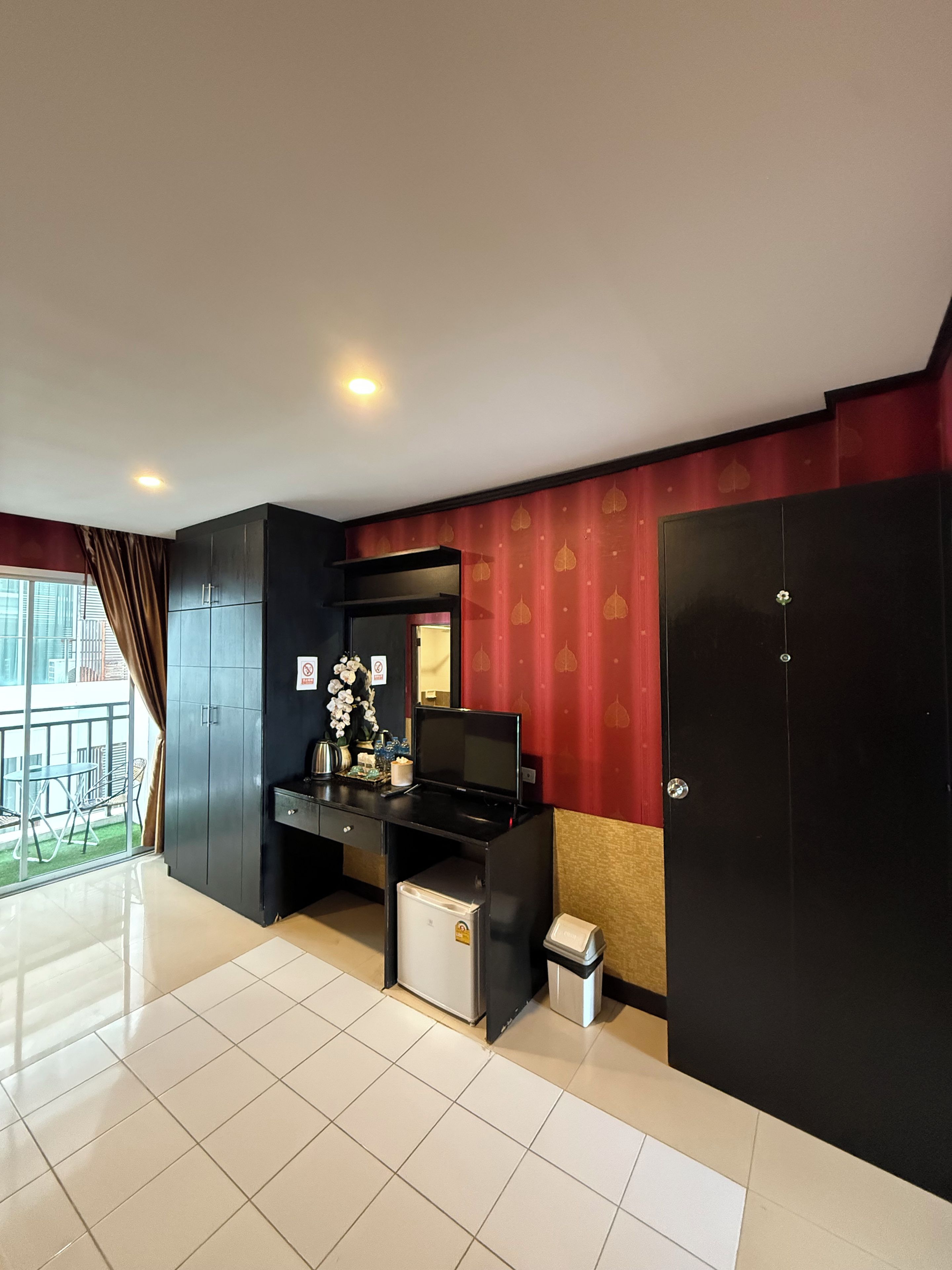 A modern room with a black desk, a small fridge, and a trash bin. There is a window with curtains, and a door with a lock.
