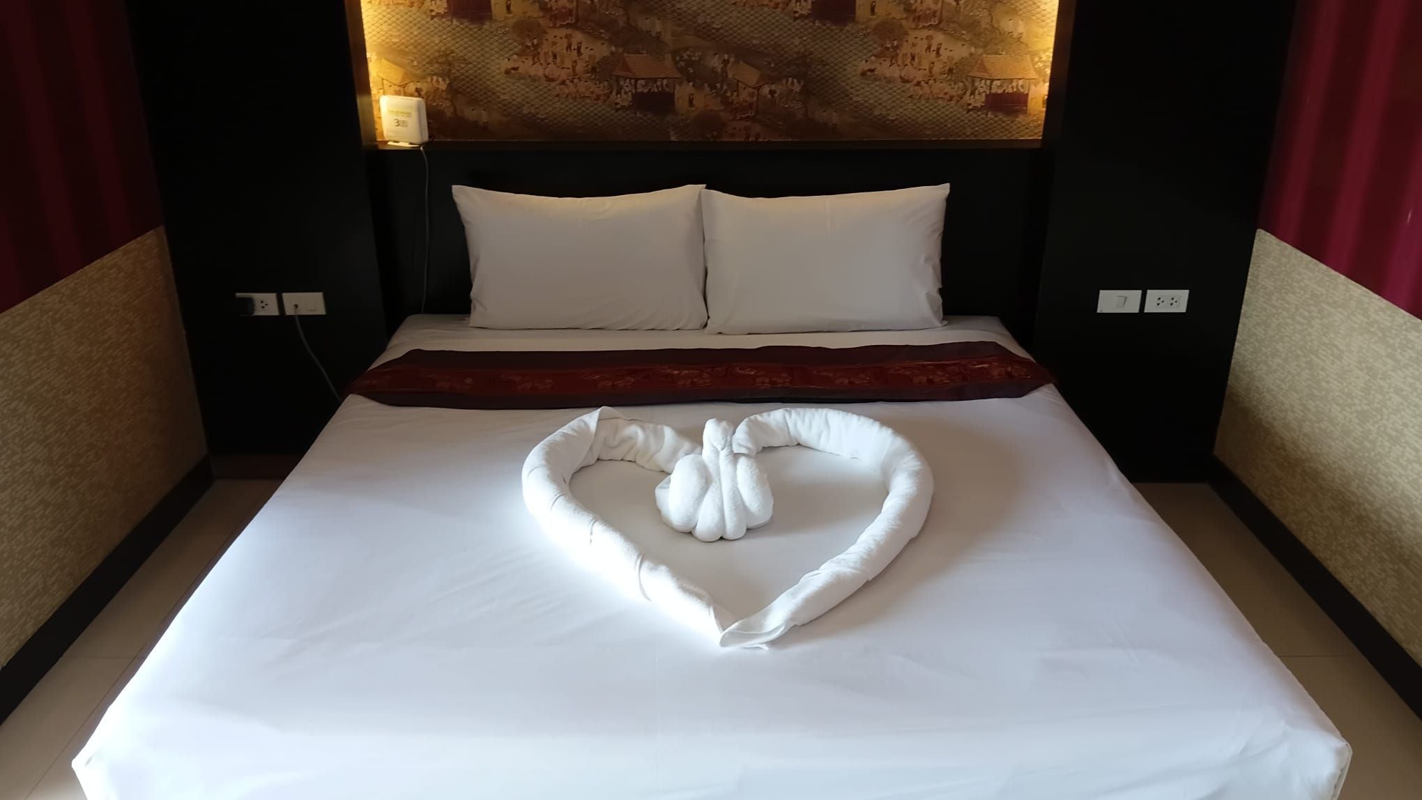 Una habitación de hotel con una colcha y almohadas en forma de corazón, impecablemente arregladas.
