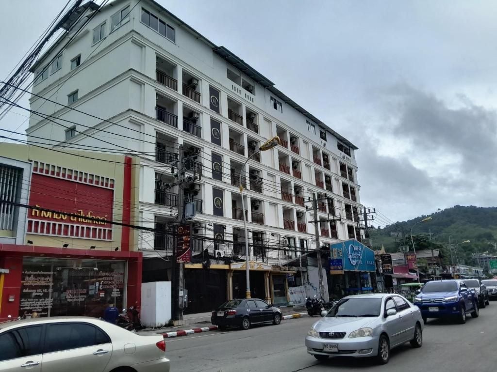 Un edificio de varios pisos con locales comerciales en la planta baja, un estacionamiento y un paisaje montañoso al fondo.