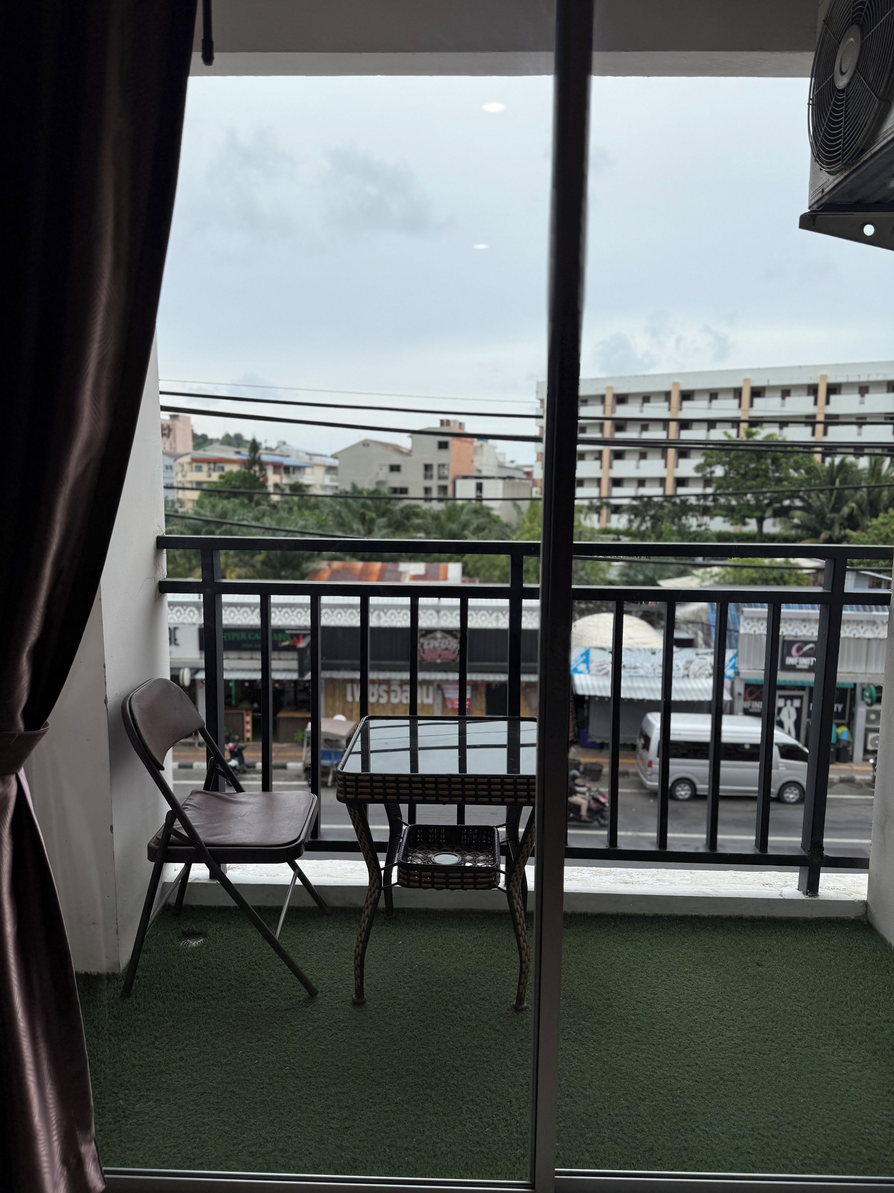 Un balcón con una silla y una mesita, vista a la calle y un edificio al fondo.