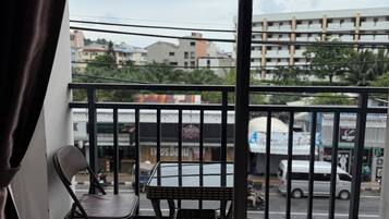 Un balcón con una silla y una mesita, vista a la calle y un edificio al fondo.