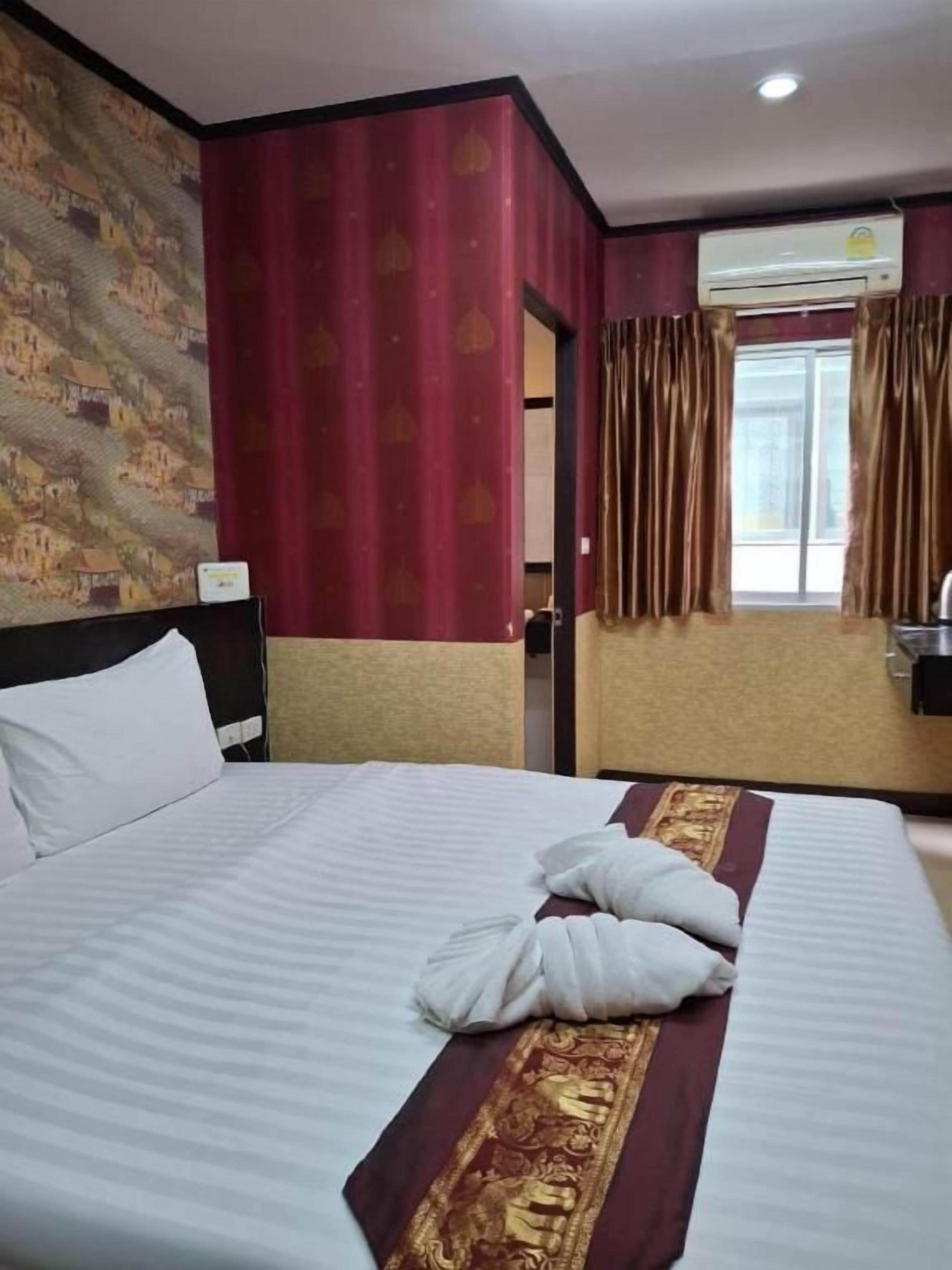 Una habitación de hotel con cama, cabecera, ventana con cortinas y unidad de aire acondicionado.