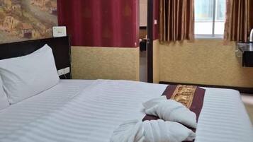 Una habitación de hotel con cama, cabecera, ventana con cortinas y unidad de aire acondicionado.
