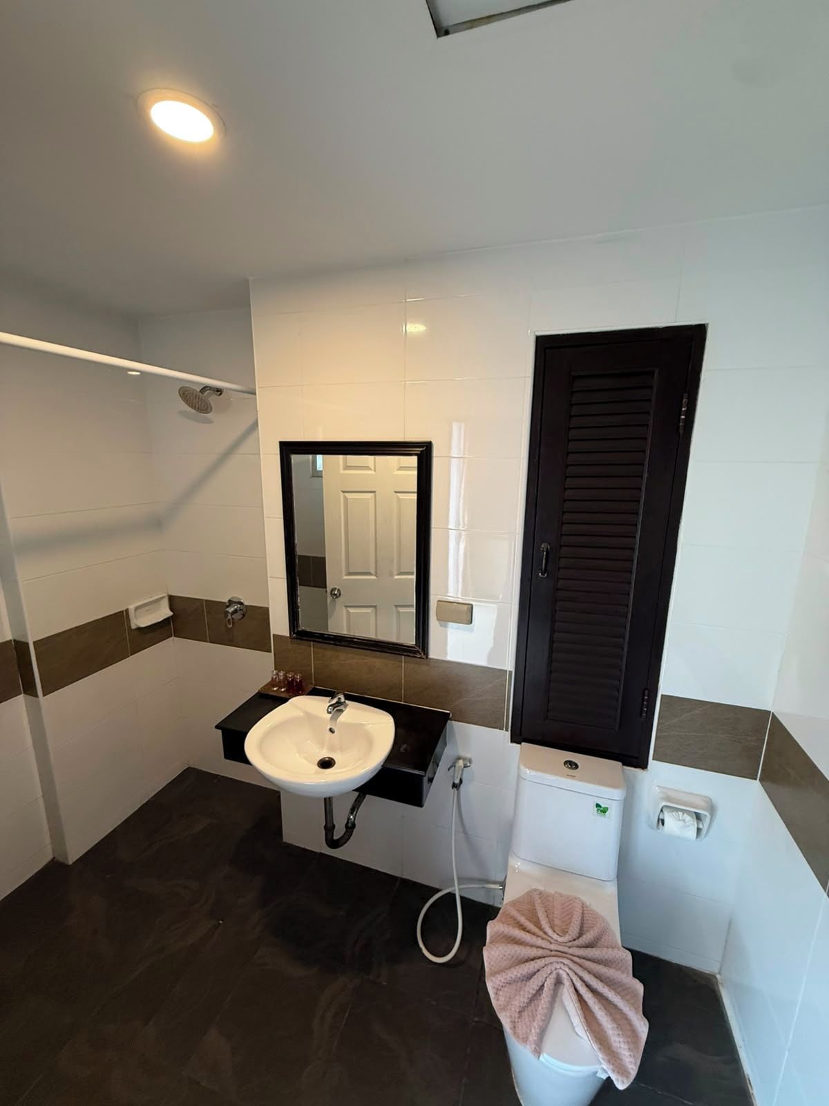 A bathroom with a white sink, a mirror, a towel, a toilet, and a shower area.
