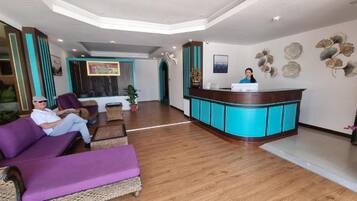 Un vestíbulo de hotel con una recepción, zona de estar con sofás morados y decoración en la pared.