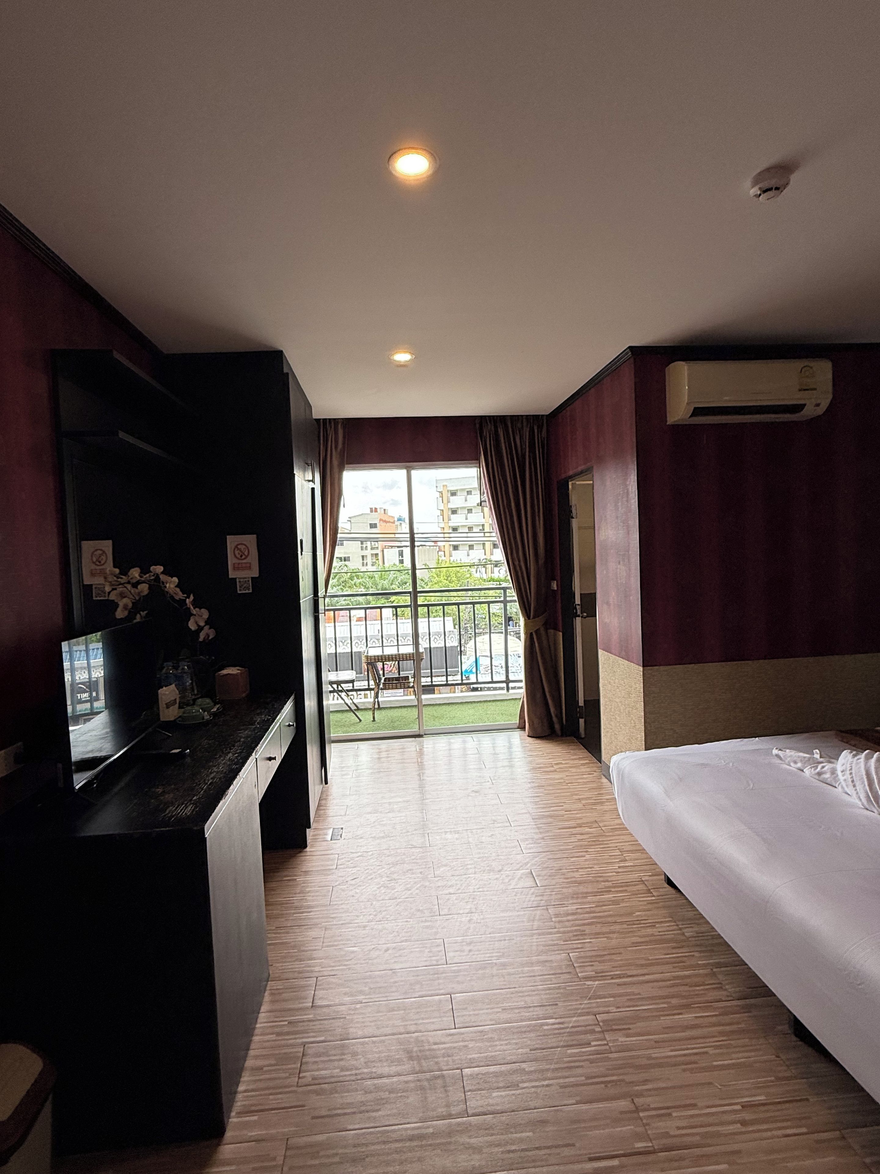 Una habitación de hotel con cama, escritorio con computadora, ventana con cortinas y aire acondicionado.