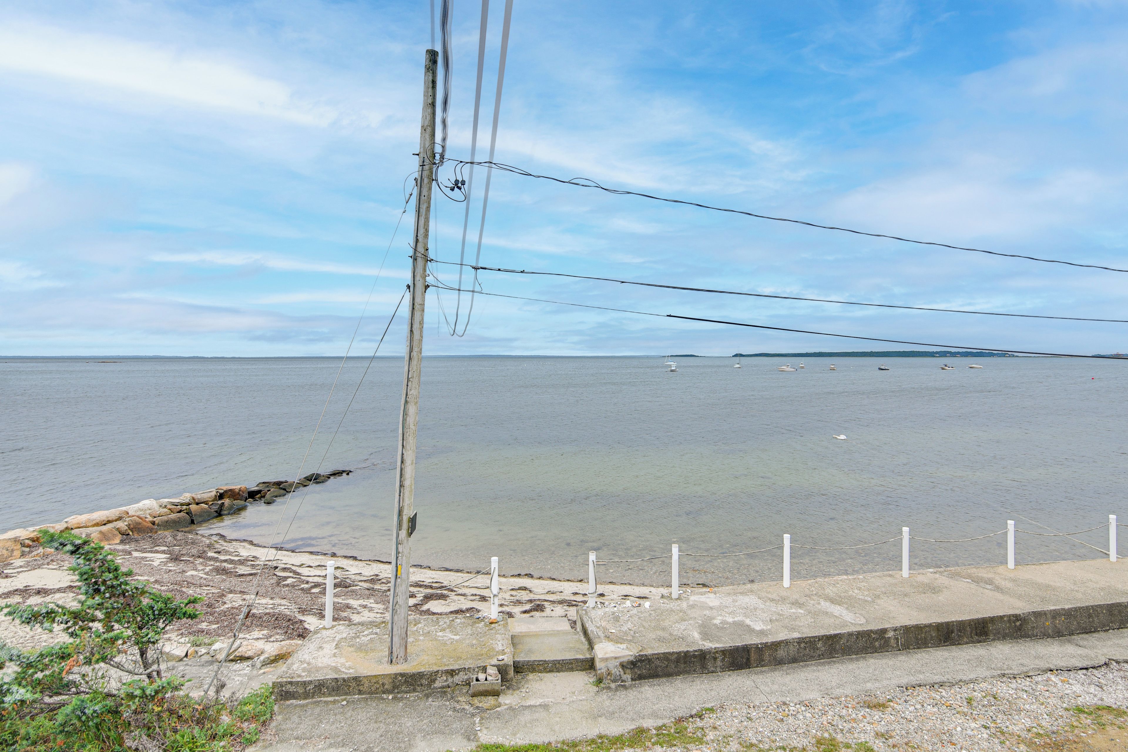 A coastal view with a concrete barrier, a wooden utility pole, and a clear sky.