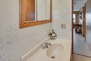 Un baño con una bañera, un espejo con marco de madera y un florero con flores sobre el lavamanos.