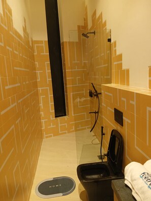 Ein kleines, schmales Badezimmer mit einem geometrischen Fliesenmuster, einer schwarzen Toilette und einem Handtuch an der Wand.
