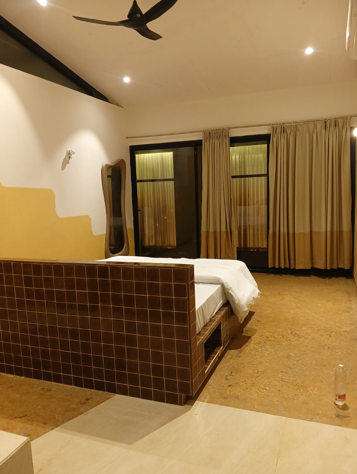 A hotel room with a bed, a ceiling fan, a window with curtains, and a tiled floor.