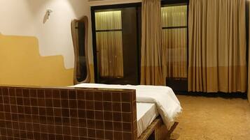 A hotel room with a bed, a ceiling fan, a window with curtains, and a tiled floor.