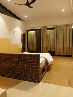 Ein Hotelzimmer mit Bett, Deckenventilator, Fenster mit Vorhängen und Fliesenboden.