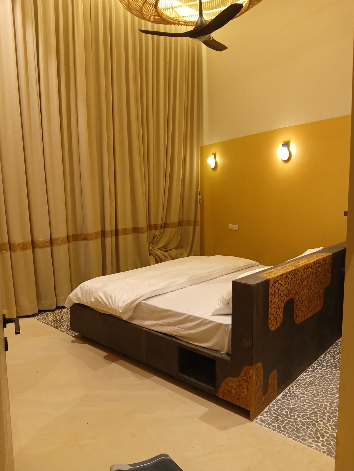 A hotel room with a bed, curtains, a wall-mounted light, and a patterned floor.