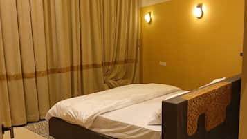 A hotel room with a bed, curtains, a wall-mounted light, and a patterned floor.