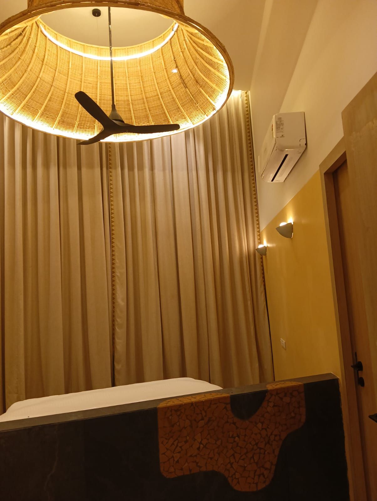 A room with a ceiling fan, a wall-mounted air conditioner, and a window with vertical blinds.