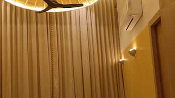 A room with a ceiling fan, a wall-mounted air conditioner, and a window with vertical blinds.
