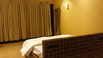 A hotel room with a bed, a wall-mounted light, and a ceiling fan.