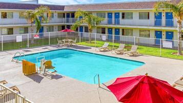 A pool area with lounge chairs and umbrellas, surrounded by a fenced pool deck.