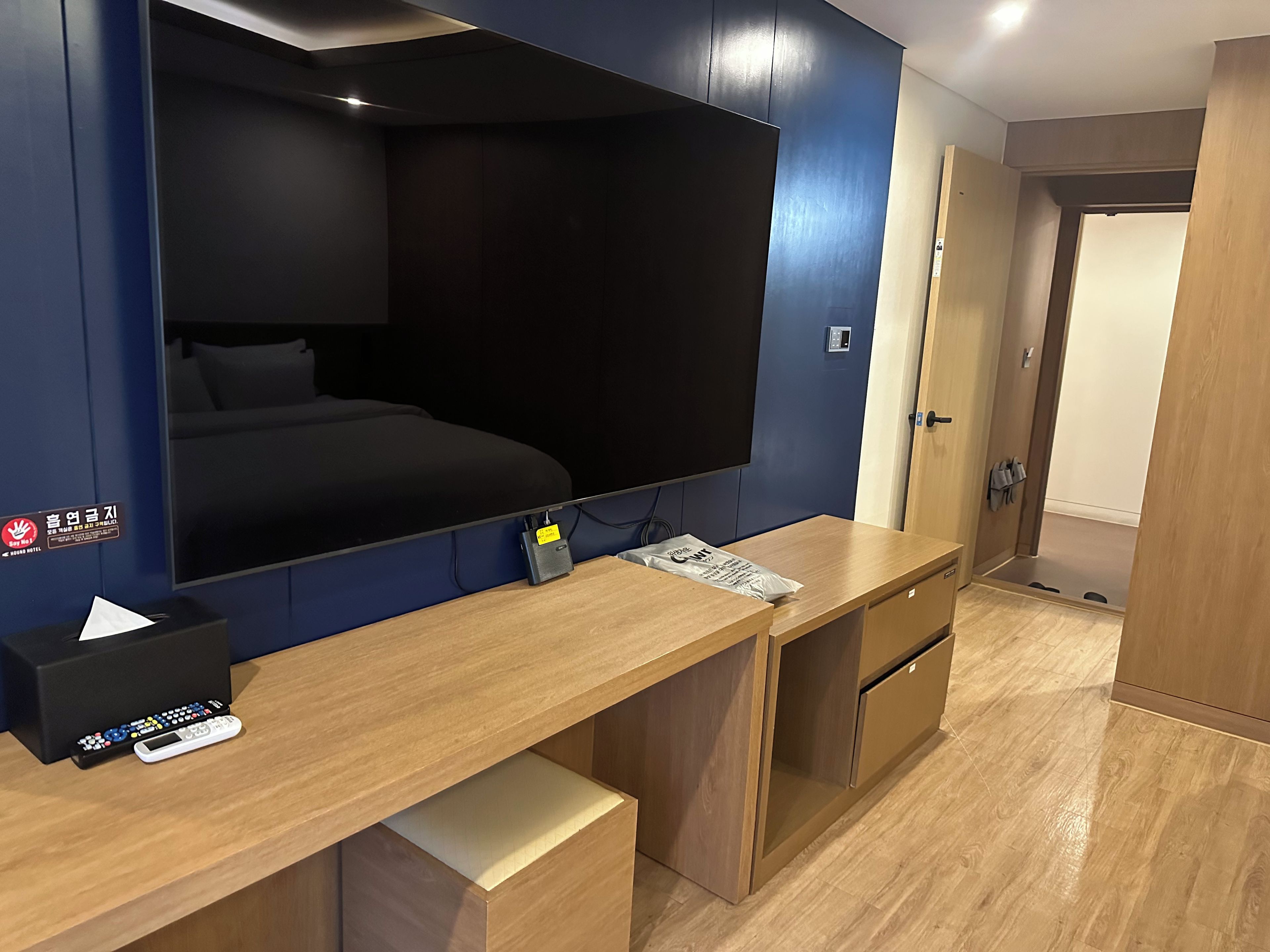 Una habitación de hotel con una cama grande, un escritorio con una computadora, un televisor de pantalla plana montado en la pared y un armario de madera.