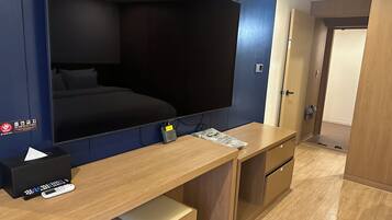 Una habitación de hotel con una cama grande, un escritorio con una computadora, un televisor de pantalla plana montado en la pared y un armario de madera.