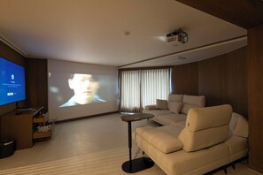 Uma sala de estar moderna com uma televisão de tela grande, um sofá, uma mesa de centro e uma tela de projetor.