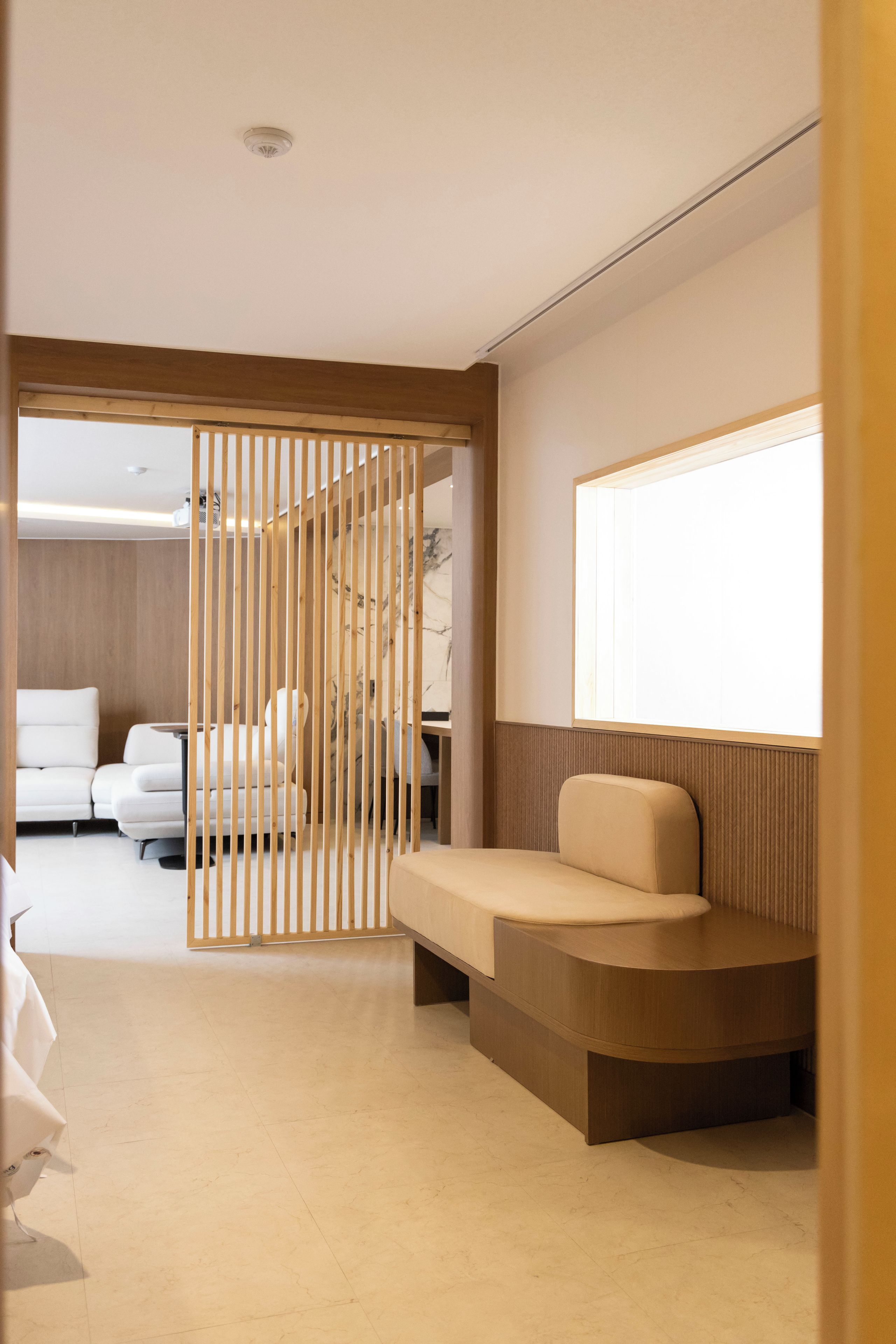 Una habitación de hotel moderna con un separador de madera, un sofá, una cama y un ventanal grande.