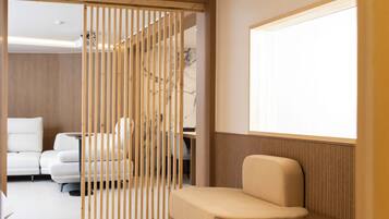 Una habitación de hotel moderna con un separador de madera, un sofá, una cama y un ventanal grande.
