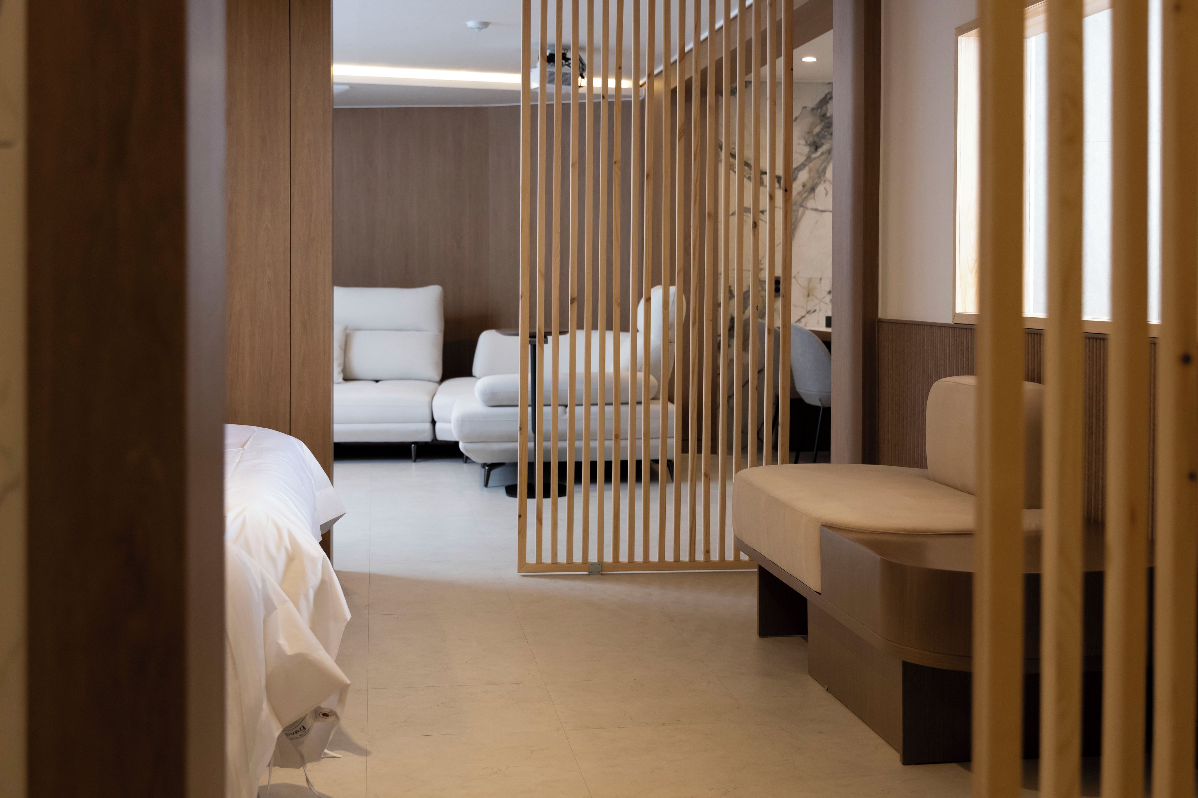 Habitación de hotel con separador de madera, sofá, cama y escritorio.