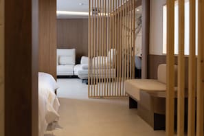 Quarto de hotel com divisória de madeira, sofá, cama e escrivaninha.