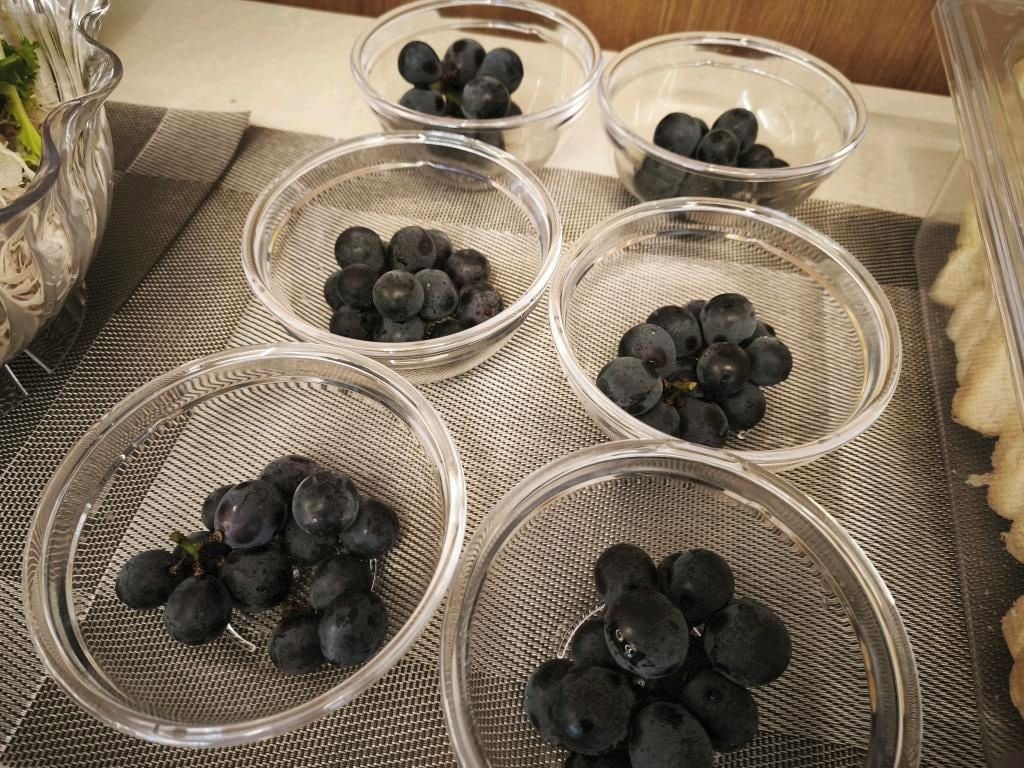 A kitchen counter with five glass bowls containing dark purple grapes.