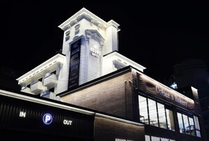 Un hotel con una torre destacada, una cafetería y un letrero que anuncia su gran inauguración.