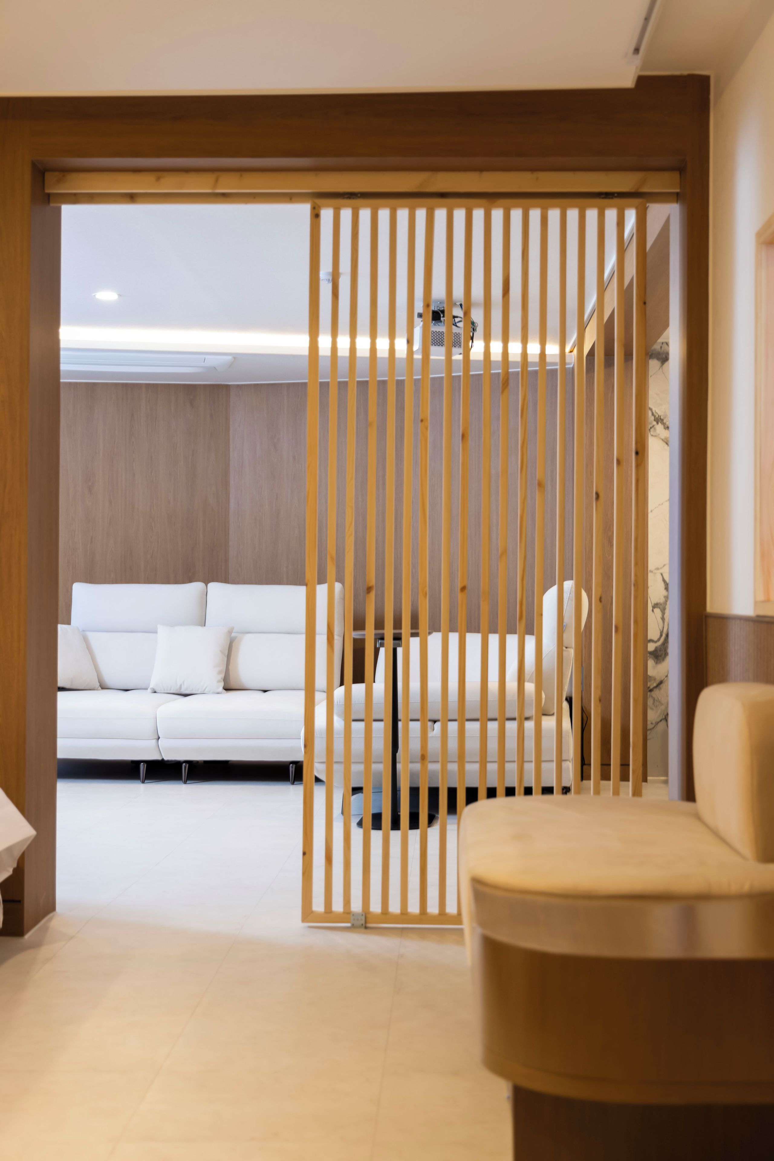 Una sala moderna con un sofá blanco, un sillón beige y un separador de madera.